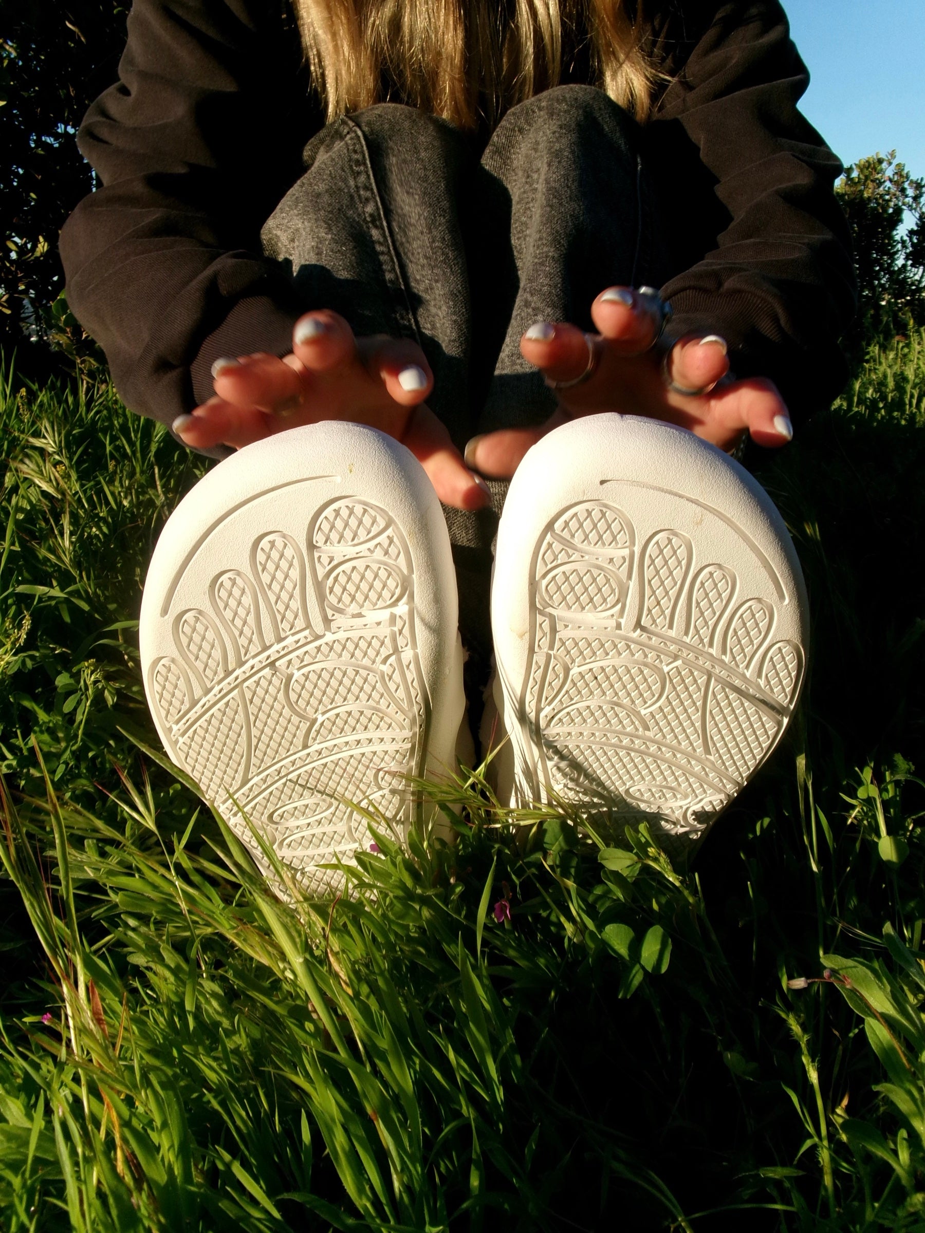 Person seated in grass with the soles of white fission.01 shoes facing the camera